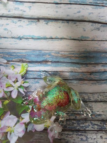 Grenouille transparente à paillettes avec des fleurs.